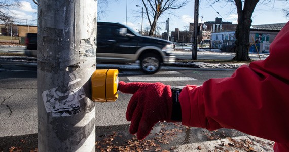 A gloved hand pushes a crosswalk button.